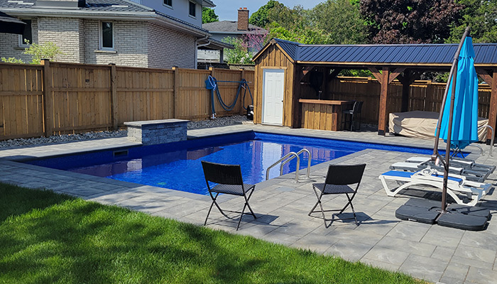 L shaped pool with bright blue lining with stamped concrete 
