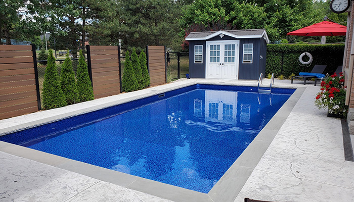 Rectangular pool with deep blue liner and grey tile coping with grey chairs 